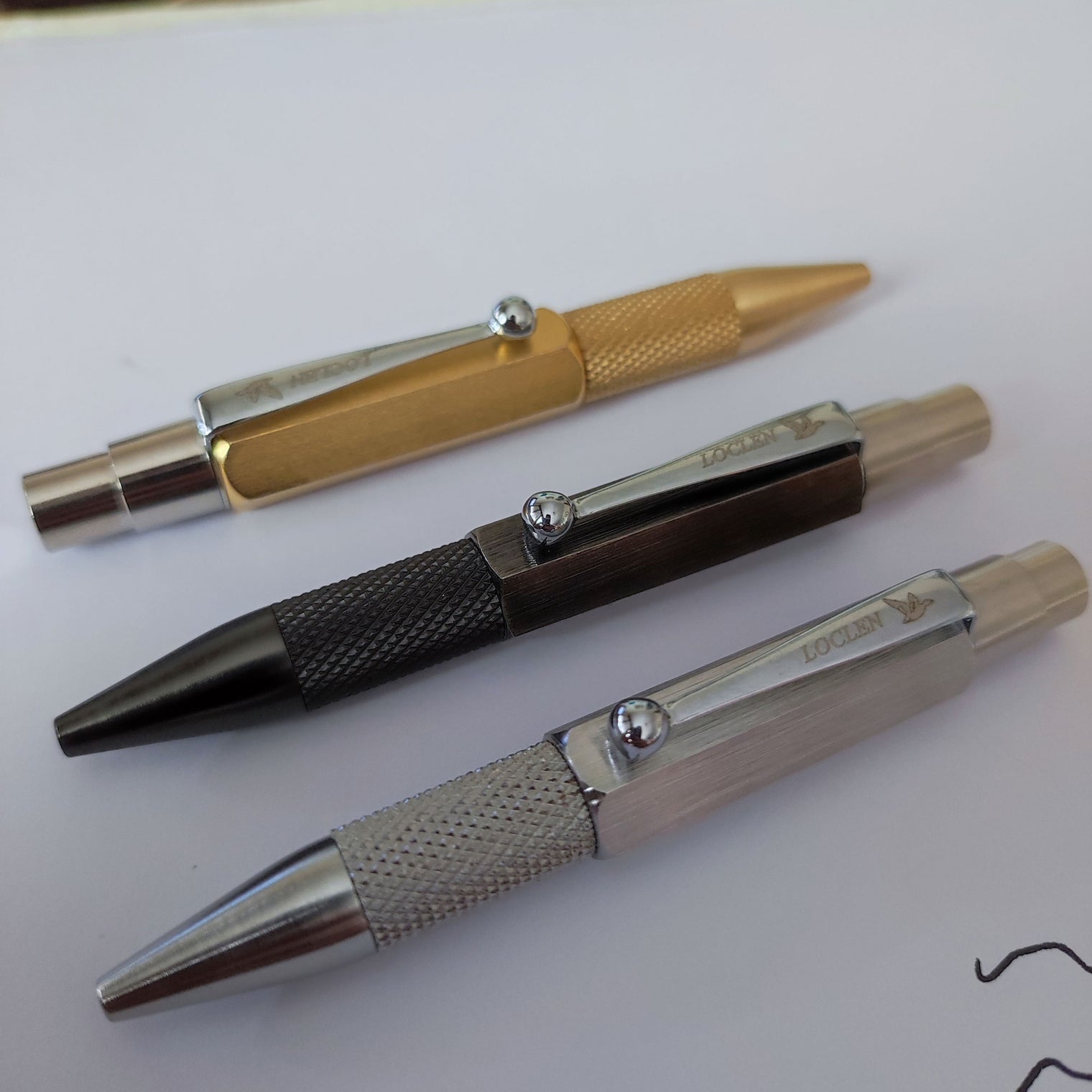 three nanetto ballpoint pens in raw brass, chrome and black sitting on a piece of paper